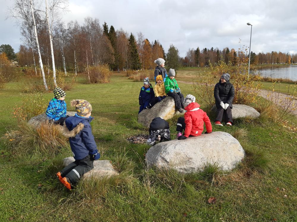 Lapsia istumassa isojen kivien päällä syksyisessä maisemassa