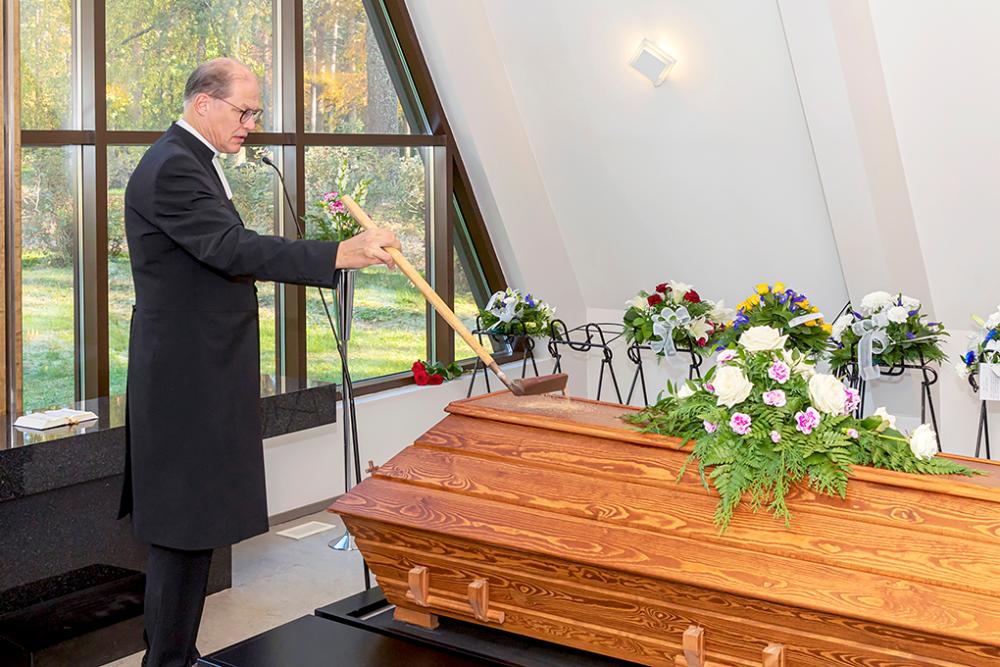 Kirkkoherra Mauno Soronen laskee hiekkaa arkun päälle hautajaisissa